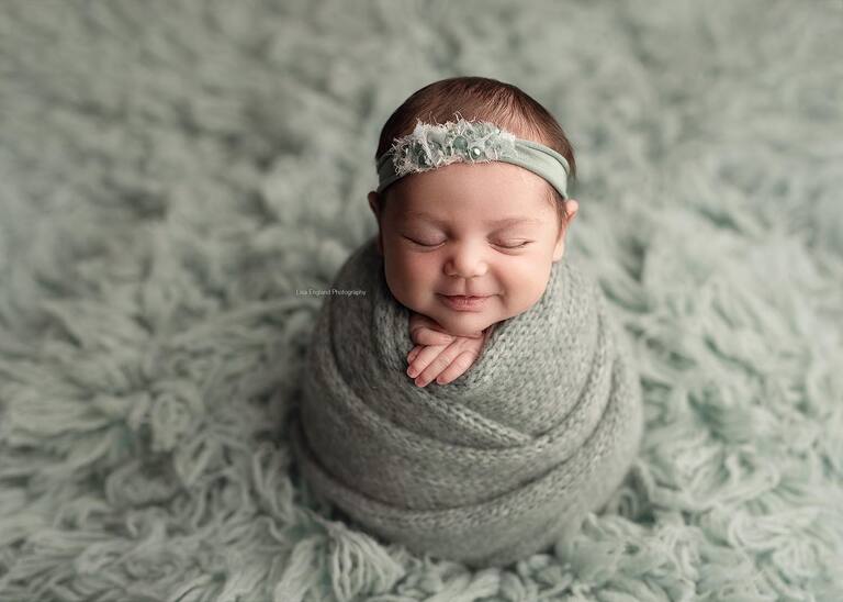 Newborn session in San Diego. Smiling newborn baby girl wrapped in sage with a pretty matching headband.