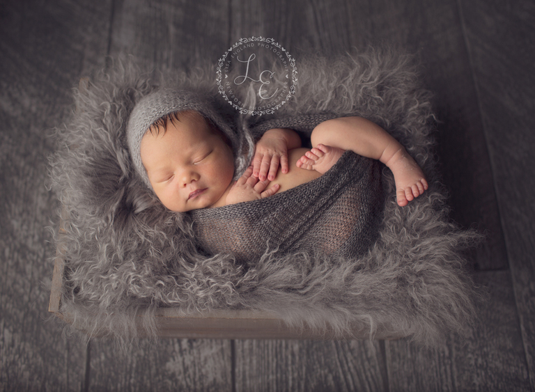 newborn snuggled up on a grey sheepskin