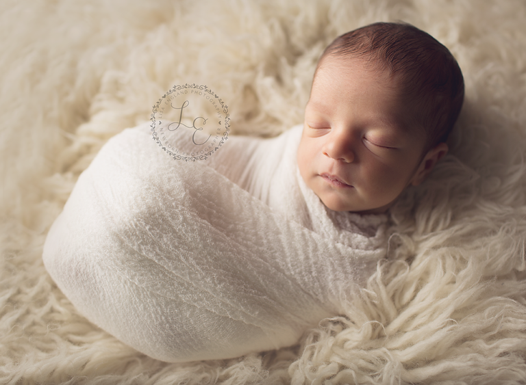 newborn boy swaddled on cream rug