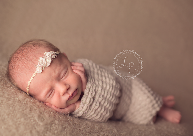 newborn girl laying on side with chin in hands
