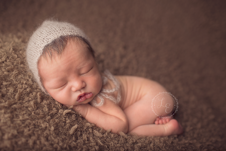 sweet baby boy wearing a tan hat on a brown backdrop