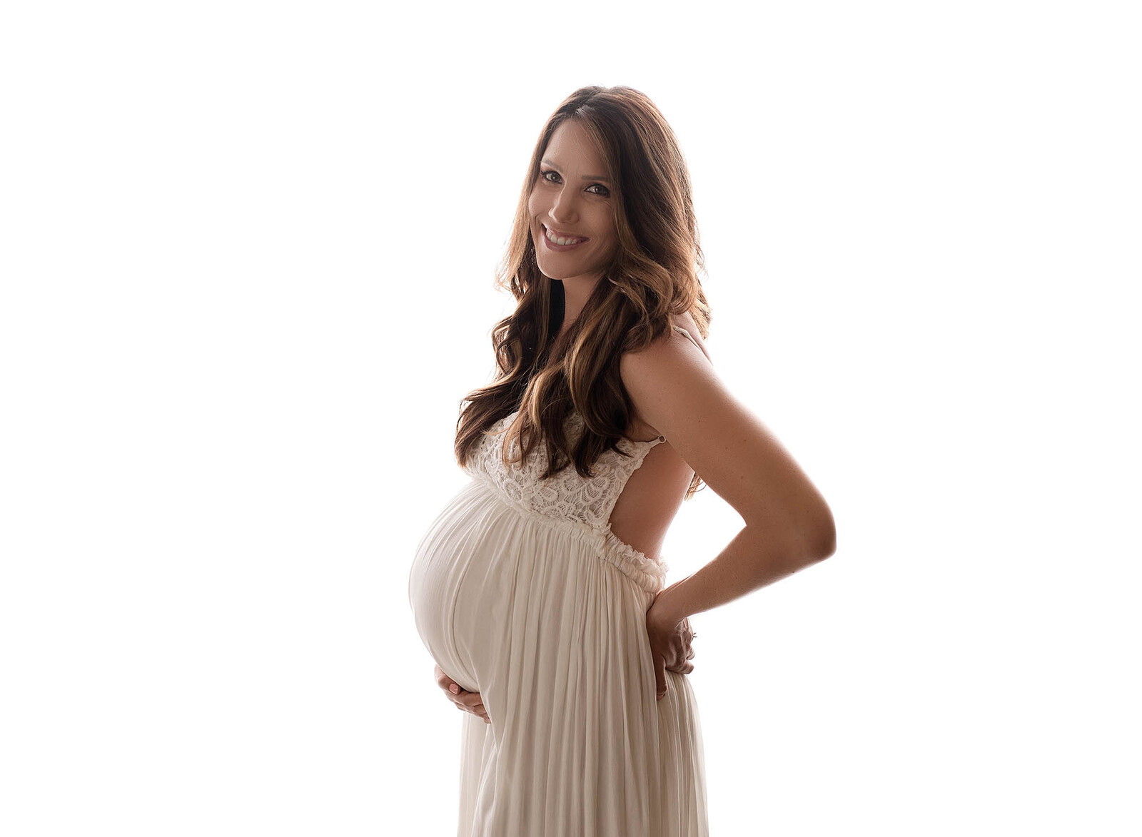 backlit maternity image of a beautiful expecting mom in a white gown
