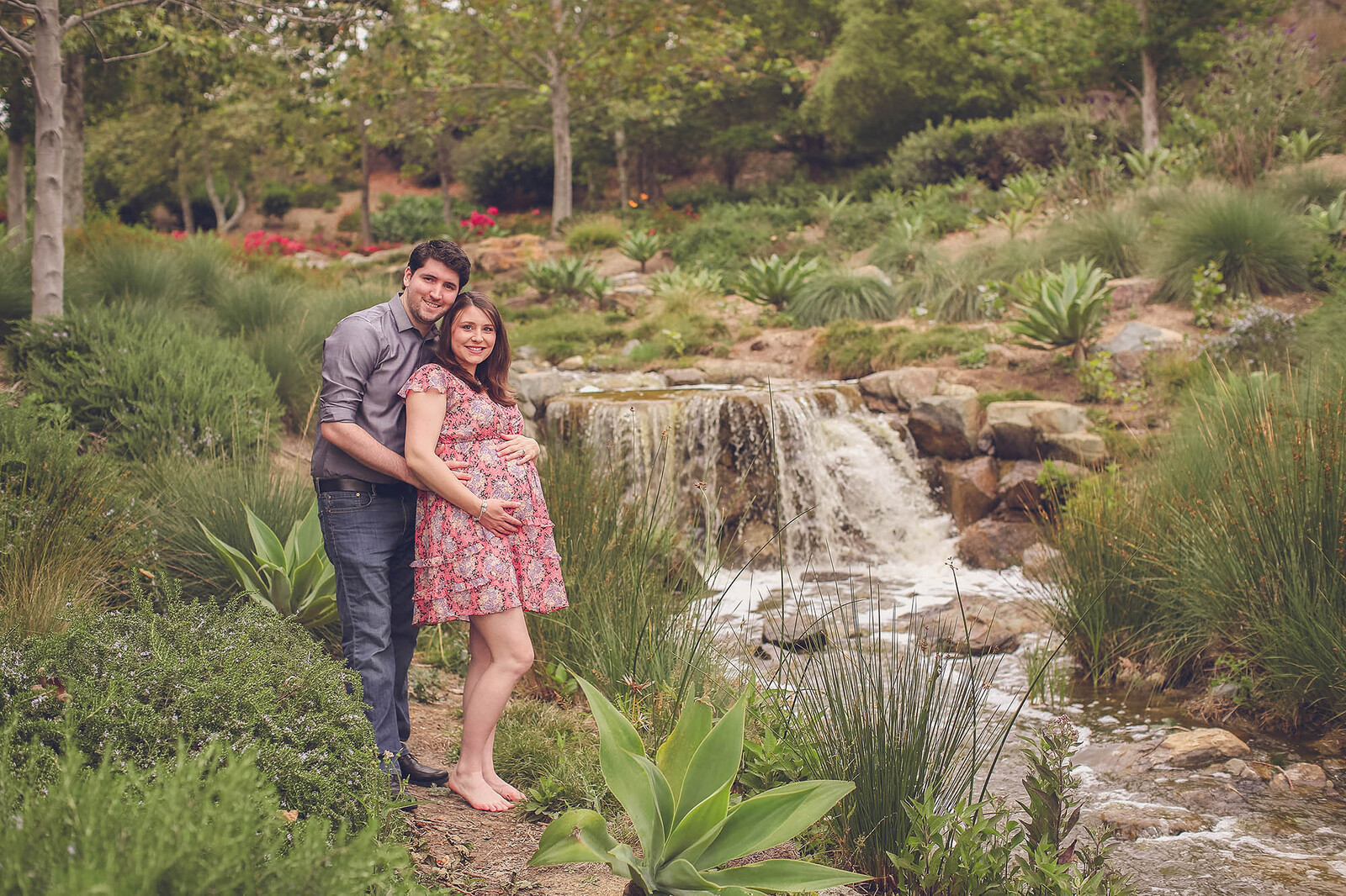 Expecting parents posed outdoors near a small waterfall