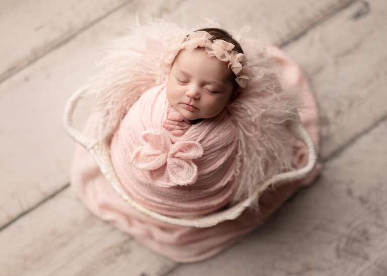 Newborn session in San Diego. Newborn girl posed in all pink asleep in a white oval basket.