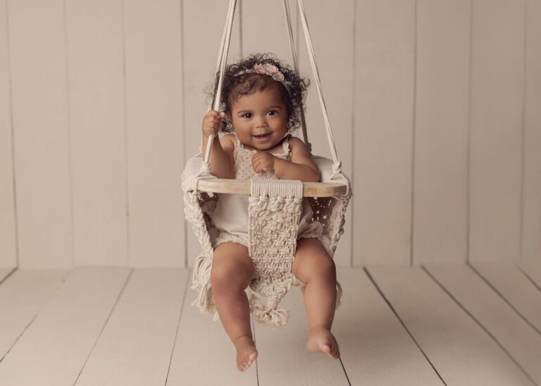 Baby milestone session. One year old girl smiling while swinging in a macrame swing.