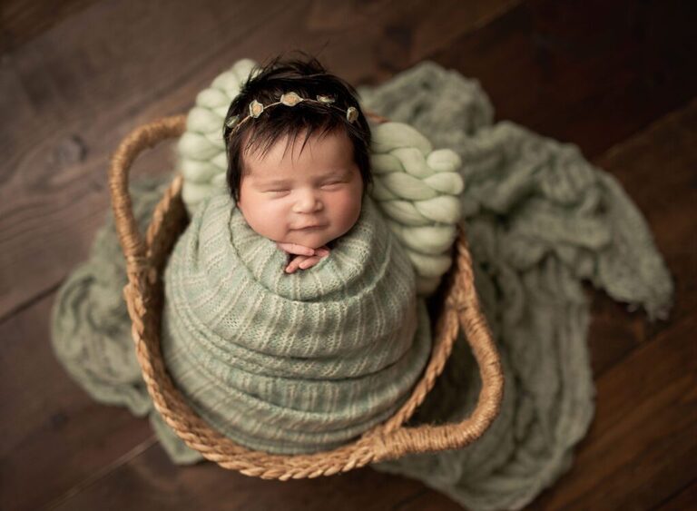 Newborn session in San Diego. Newborn girl wrapped in sage sleeping in a oval basket.