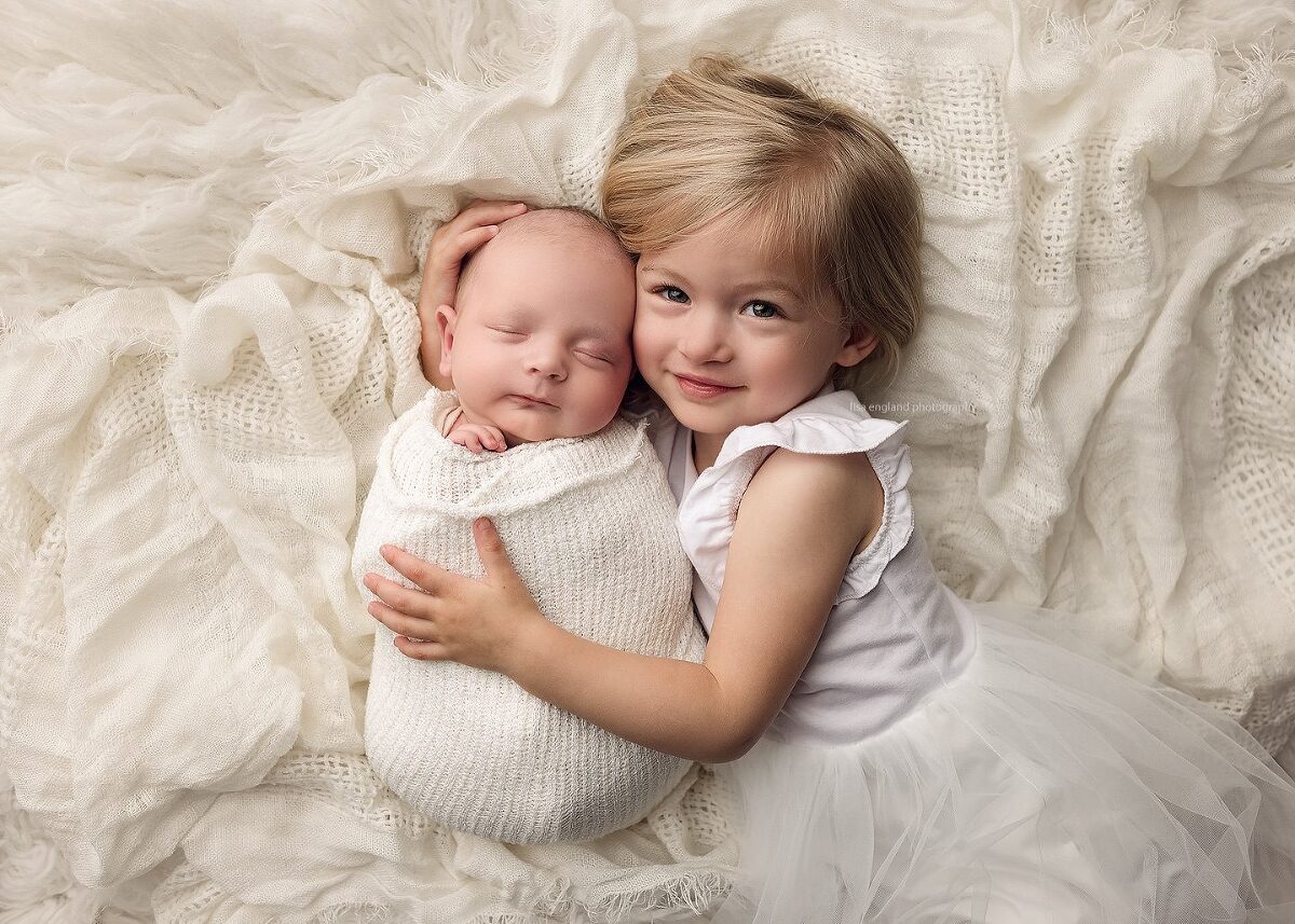 big sister cuddling with her new baby sister in an all white set up - Lisa England Photography, San Diego lifestyle newborn photography