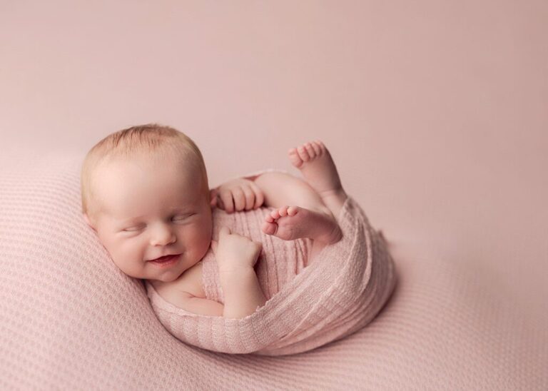 smiley newborn swaddled in a pink wrap during her session with Lisa England Photography in San Diego