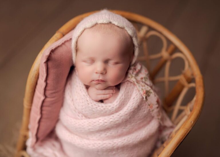baby girl wrapped in pink sleeping in a bamboo chair prop during her session with Lisa England Photography
