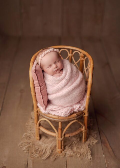 baby girl wrapped in pink sleeping in a bamboo chair prop during her session with Lisa England Photography