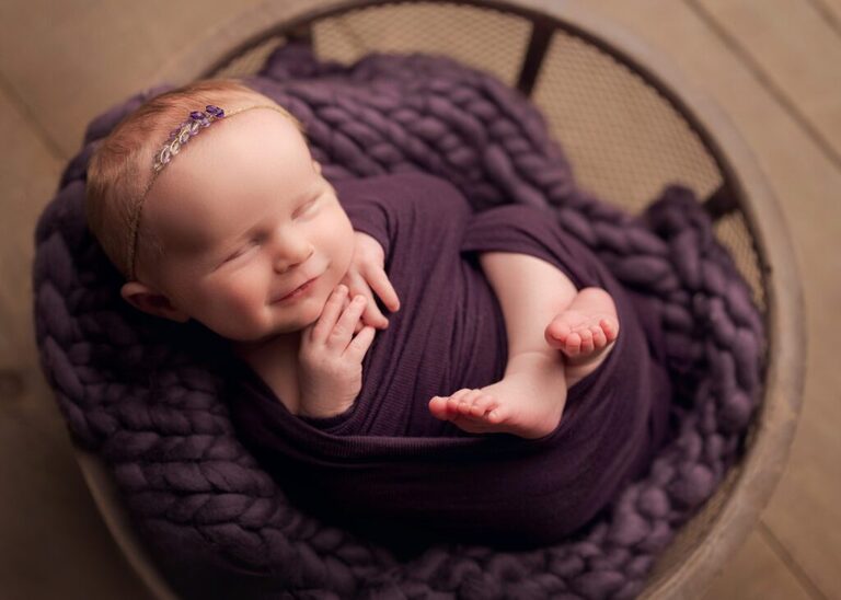baby girl wrapped in purple sleeping in a bowl