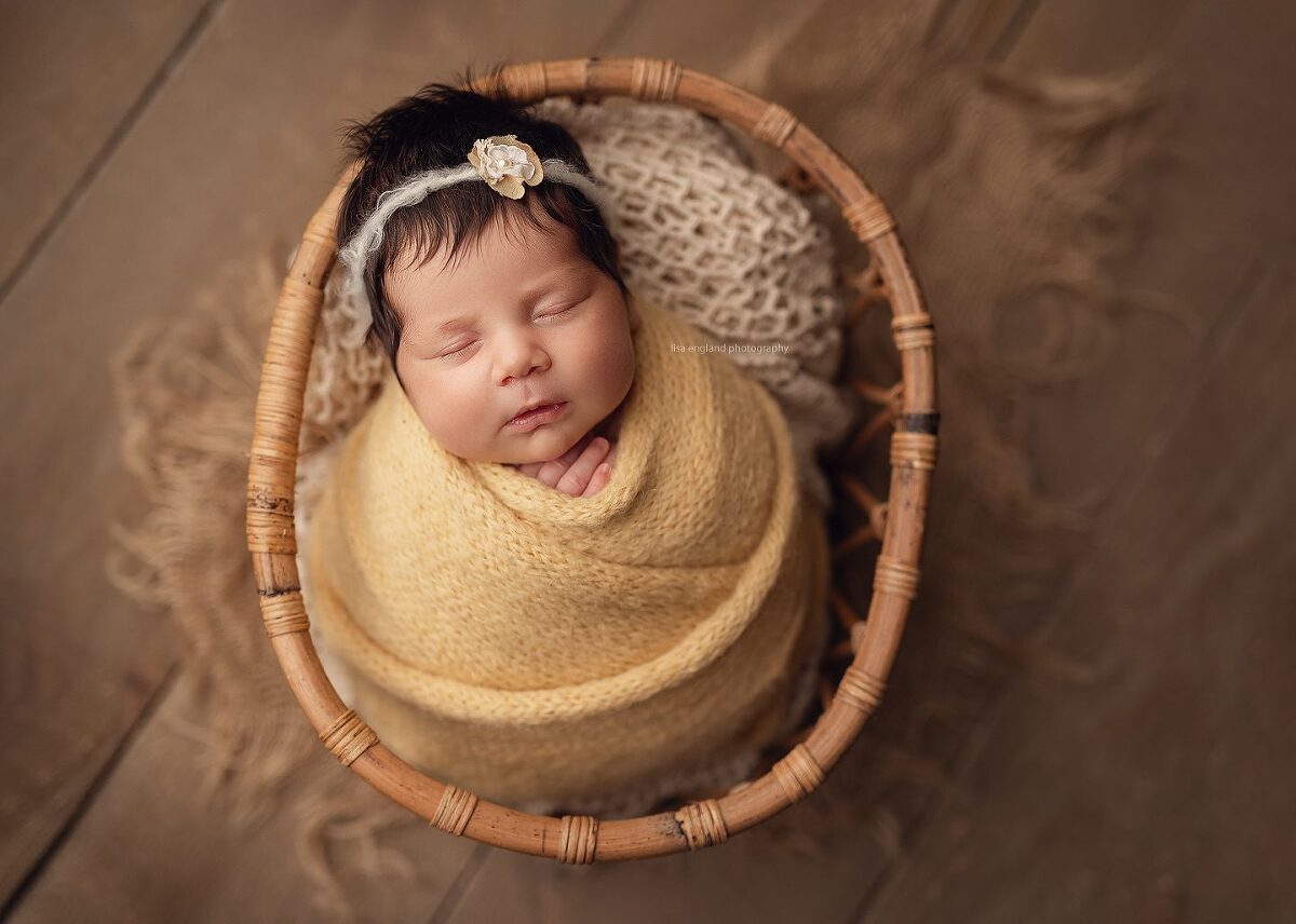 newborn baby girl sleeping in a basket, wrapped in a yellow wrap