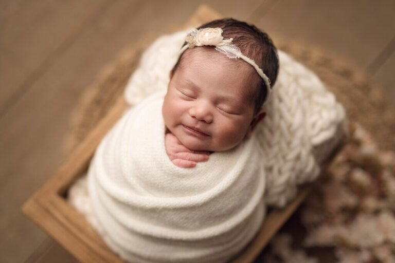 Beautiful, sleepy baby girl wrapped in a soft cream wrap during her session in San Diego