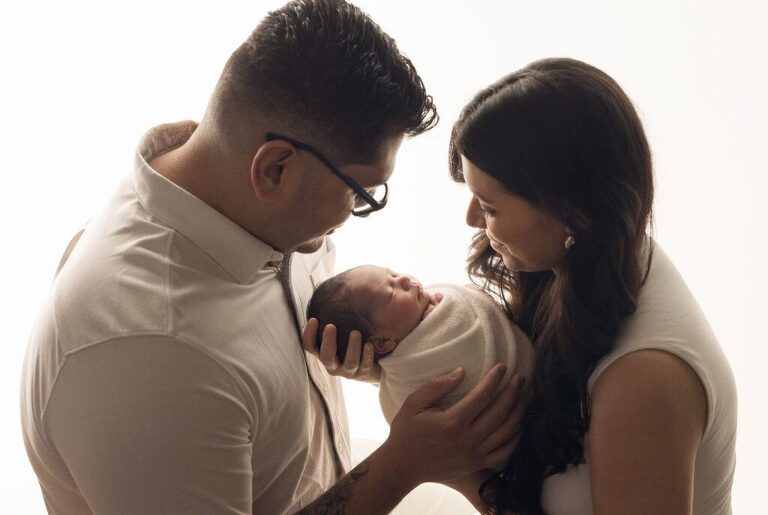 Beautiful backlit parents posed with their new baby girl during her newborn session in San Diego