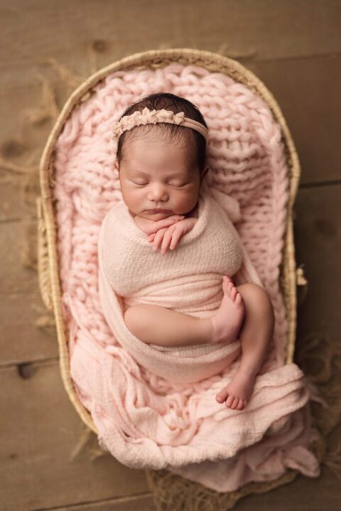 Sleepy baby girl wrapped in a soft pink wrap during her newborn session in San Diego