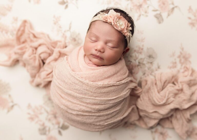 Baby girl wrapped in light pink sleeping on a pretty floral fabric. San Diego Newborn Photographer