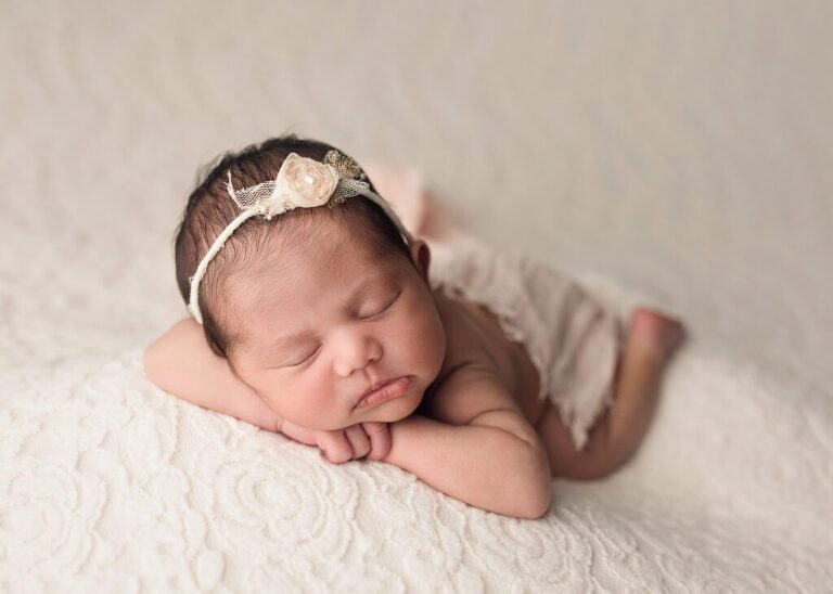 Gently posed baby fast asleep on a soft white blanket during her newborn session in San Diego