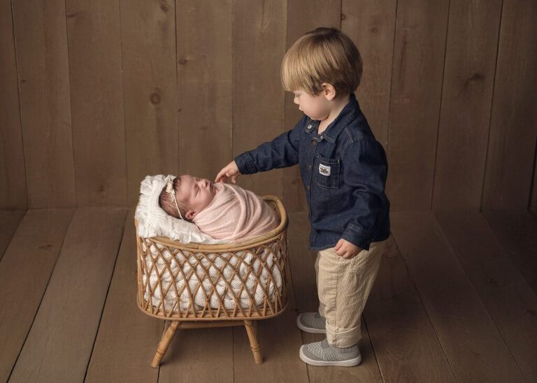 two year old brother standing proudly next to newborn baby sister